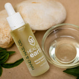 pinotage therapy hand and nail oil, 30 ml, rested on rocks with a bowl of oil next to it